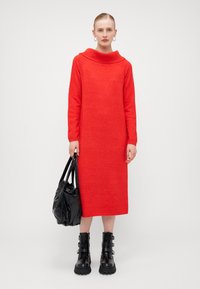 Abito in maglia rosso a maniche lunghe con scollo ampio e arrotondato. Abbinato a una borsa nera lucida e stivali neri chunky con fibbie.