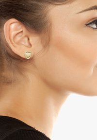 Orecchini a stud a forma di cuore in oro esposti all'orecchio di un modello. Il design presenta una superficie liscia e lucida con una curvatura sottile.