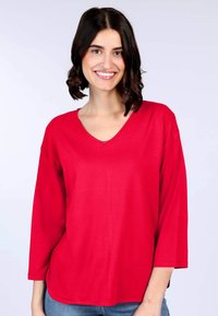 Rotes V-Ausschnitt-Oberteil mit drei Viertelärmeln, aus weichem Stoff gefertigt; glatte Textur, lockere Passform und abgerundeter Saum am Boden.