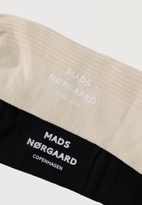 Μπάντες υφάσματος σε μπεζ και μαύρο με ραβδωτή υφή, καθεμία τυπωμένη με το κείμενο «MADS NØRGAARD COPENHAGEN» σε άσπρο χρώμα.