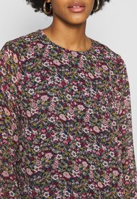 Blommig blus med ett färgglatt mönster av rosa, vita och gröna blommor på en mörkblå bakgrund; lättviktig tyg och rundad halsringning.