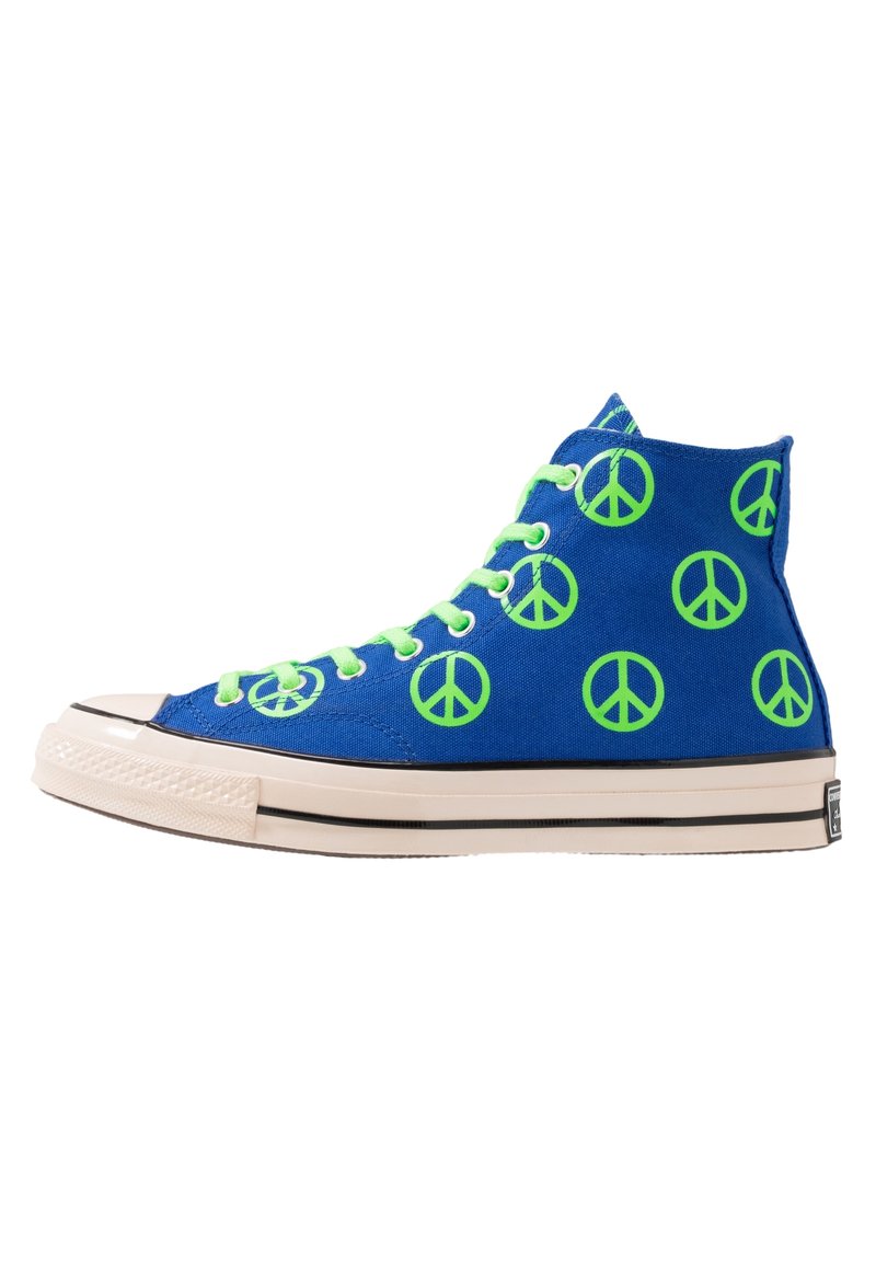 High-top sneakers in blue canvas with green peace sign patterns, featuring white rubber soles and green laces. Black stripe along the sole.