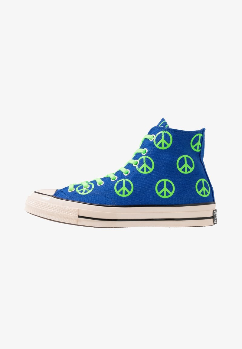 High-top sneakers in blue canvas with green peace sign patterns, featuring white rubber soles and green laces. Black stripe along the sole.