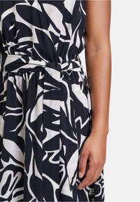 Ärmelloses Kleid in Marineblau und Weiß mit abstrakten Mustern, ausgestattet mit einem Taillengürtel und einem plissierten Design. Weicher Baumwollstoff mit fließender Silhouette.