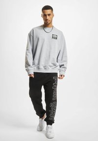 Šedá mikina s logem a černé tepláky s bílým textem na boku. Bílé tenisky doplňují ležérní outfit.