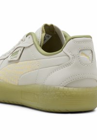 A Puma Palermo sneaker világoskrém bőr felsőrésszel, texturált sárga pöttyös mintával, zöld részletekkel és áttetsző zöld talppal rendelkezik.