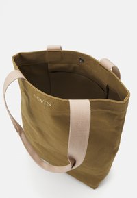 Torebka na zakupy z płótna w oliwkowej zieleni z jasnobeżowymi uchwytami. Posiada fakturę z kropek oraz haftowane logo. W środku znajduje się jedna kieszeń.