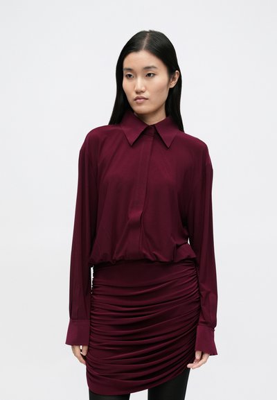 Ilga rankovėmis bordo spalvos palaidinė su sulankstytu apkaltu, derinama su raukiniu sijonu. Lygus audinys su šiek tiek blizgiu paviršiumi.