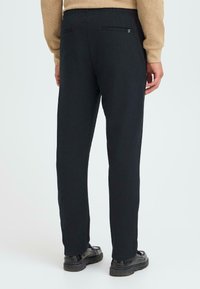 Musta housut tekstuurilla, istuva suora malli, kaksi takataskua ja joustava vyötärö, yhdistetty mustiin kenkiin.