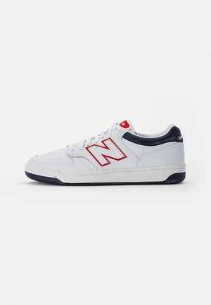 Sneaker bianco a taglio basso con logo rosso "N", collare posteriore nero, lacci bianchi e suola nera su sfondo chiaro uniforme.