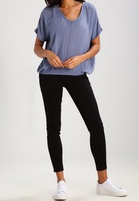 Lyseblå kortærmet bluse med V-hals, kombineret med sorte skinny jeans og hvide sneakers. Glat stof med en afslappet pasform.