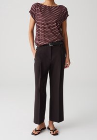 Mønstret bluse med korte ærmer i maroon med bådudskæring, parret med sorte vide bukser og flade sorte sandaler. Enkel, skr æddersyet design.