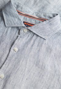 Camisa de manga corta a rayas azul y blanca con cuello abotonado, con botones blancos y una etiqueta con la marca "Superdry".