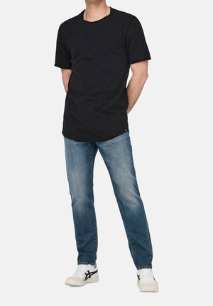 Schwarzes T-Shirt mit kurzen Ärmeln und rundem Ausschnitt, kombiniert mit hellblauen Jeans und weißen Sneakers mit schwarzen Akzenten.