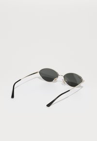 Gafas de sol metálicas en forma ovalada con lentes oscuros, delgada montura plateada y patillas de plástico negro. Cuenta con almohadillas para la nariz para mayor comodidad.