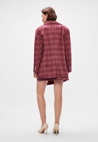 Plaid blazer in shades of burgundy and pink, featuring a fitted silhouette, wide lapels, and decorative buttons on the sleeves.