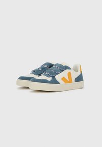 Modré semišové tenisky s bílými koženými doplňky, vybavené suchými zipy a oranžovým logem ve tvaru V. Texturovaný svršek a gumová podrážka.