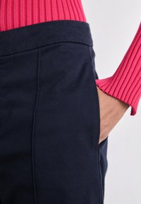 Námořnické kalhoty s hladkou texturou, s bočními kapsami a upraveným střihem, v kombinaci s jasně růžovým žebrovaným svetrem s manžetami.