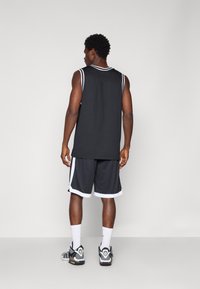 Jersey deportivo sin mangas negro con ribetes blancos, combinado con pantalones cortos de baloncesto negros con acentos blancos y zapatillas deportivas negras.