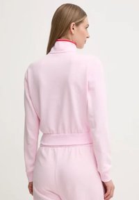 Giacca zip-up rosa chiaro realizzata in tessuto morbido, con colletto alto accentato in rosso, vita elastica e maniche lunghe con polsini aderenti.
