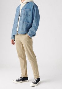 Jeansjacka i ljusblått med knappstängning och två framfickor, kombinerad med khakibyxor och svarta högskaftade sneakers.