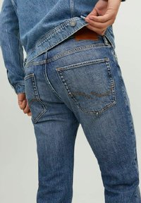 Jeans de mezclilla azul con un primer plano de los bolsillos traseros, que muestran costuras visibles, un parche de cuero de la marca y una textura ligeramente desgastada.