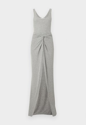 Γυναίκα με γκρι αμάνικο μακρύ φόρεμα με σκίσιμο στο μπροστινό μέρος και λεπτομέρεια κόμβου, κρατάει μαύρη τσάντα χειρός και φοράει μαύρες μπαλαρίνες, στέκεται σε λευκό φόντο.