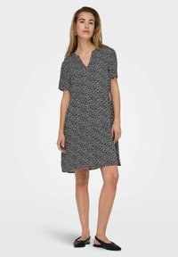 Schwarzes Kleid mit einem Blattmuster, kurzen Ärmeln, V-Ausschnitt und lockerer Passform. Kombiniert mit schwarzen Slingback-Ballerinas. Glatte Textur.