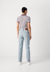 Lichtblauwe spijkerbroek met een relaxte pasvorm, voorzien van achterzakken en een leren merklabel op de tailleband. Gestreept poloshirt in beeld.