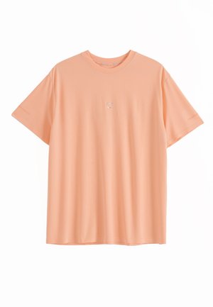 Pfirsichfarbenes T-Shirt mit kurzen Ärmeln und rundem Ausschnitt, mit kleinem weißen, auf der Brust zentriert gesticktem Text.