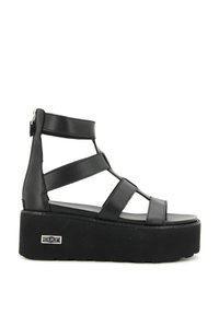 Sandali con piattaforma nera caratterizzati da molteplici cinturini e una chiusura con zip sul retro. La suola è strutturata e solleva il piede.