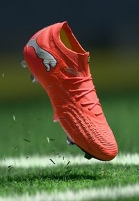 Leuchtend orangefarbener Fußballschuh mit strukturiertem synthetischem Material, verfügt über ein schlankes Design, Schnürsenkel und ein markantes Logo an der Seite.