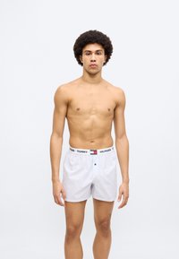 Λευκά μπόξερ με ρίγες και ελαστική μέση με λογότυπο. Διαθέτουν κλείσιμο με ένα κουμπί και χαλαρή, άνετη εφαρμογή.