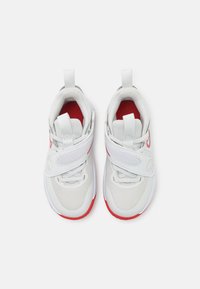 Białe buty sportowe z czerwonymi akcentami, siateczkowa cholewka, zapięcie na rzep, zaokrąglony nosek, wyściełany kołnierz i teksturowana kauczukowa podeszwa.