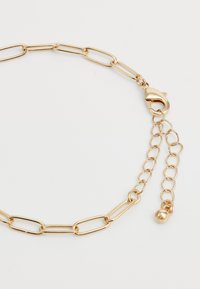 Gold chain bracelet with elongated links, lobster clasp, and adjustable short chain ending with a small round charm on a white background.