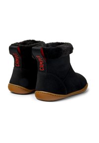 Botas de tobillo de ante negro con forro de piel sintética, suelas de goma marrón y acentos rojos del logo en el talón. Textura suave con forma redondeada.