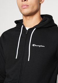 Felpa nera con zip realizzata in misto cotone, dotata di un logo bianco sul lato sinistro del petto e di lacci bianchi sul cappuccio.