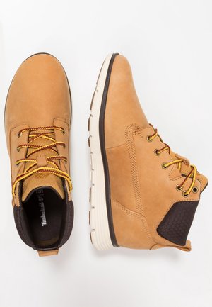 Lichtbruine leren bergschoenen met gele en rode veters, zwarte gewatteerde kraagjes en witte rubberen zolen, weergegeven vanuit boven- en zijaanzichten.