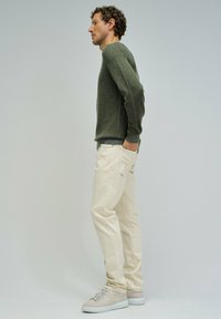 Lekki, oliwkowy sweter, okrągły dekolt; w zestawieniu z kremowymi spodniami; nosi beżowe trampki; gładka tekstura, luźny krój.