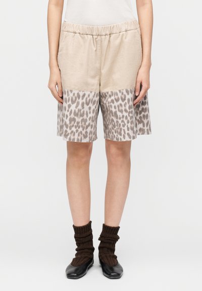 Shorts beiges avec une taille élastique, comportant un panneau inférieur à imprimé léopard. Texture douce, coupe au-dessus du genou, assortis à des chaussures noires et des chaussettes brunes.
