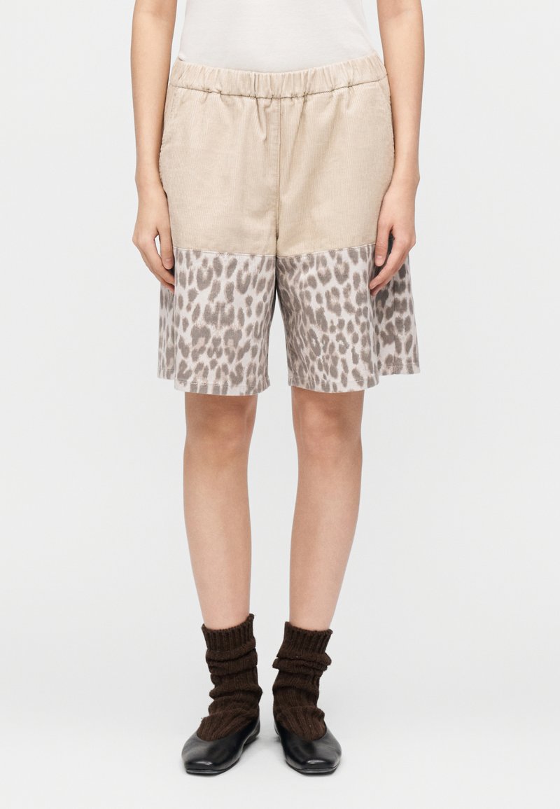 Μπεζ σορτς με ελαστική μέση, με πάνελ κάτω μέρος με λεοπάρ σχέδιο. Μαλακή υφή, μήκος μέχρι το γόνατο, συνδυασμένα με μαύρα παπούτσια και καφέ κάλτσες.