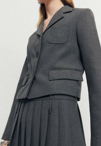 Szara dopasowana marynarka o skróconym kroju, z dwoma przednimi kieszeniami, trzema guzikami i gładką fakturą.