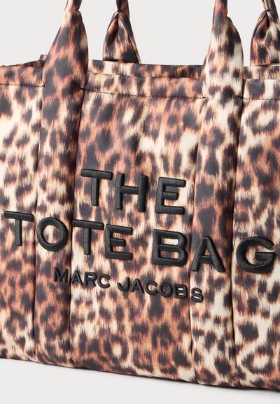 Sac fourre-tout imprimé léopard avec texte brodé noir "THE TOTE BAG MARC JACOBS" et deux poignées rembourrées sur un fond uni.