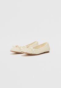 Bailarinas en material tejido crema con punta redondeada, lazo decorativo y sutiles acentos dorados. Suela plana para mayor comodidad.