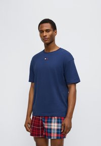 Μπλε βαμβακερό t-shirt με κοντά μανίκια και μικρό λογότυπο στο στήθος, συνδυασμένο με καρό σορτς σε αποχρώσεις κόκκινου και μπλε.