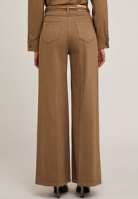 Brown, wide-leg trousers with a smooth texture, featuring two back pockets and a high waistband, complemented by a thin belt.