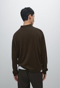 Brown long-sleeve polo shirt with a relaxed fit, made from soft fabric, featuring a collar and visible stitching on the shoulders.