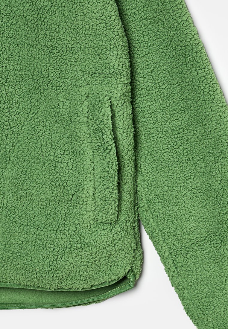 Groene fleecejack met een zachte, gestructureerde oppervlakte, voorzien van een voorzak en een afgeronde zoom aan de onderkant.
