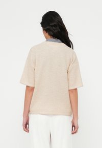 Beige, kortærmet sweater med løs pasform. Blødt, tekstureret stof. Har en synlig grå- og hvidternet krave under.