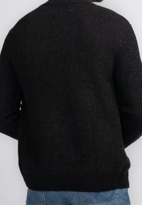 Mörkgrå stickad tröja med strukturerad yta, med rund hals och ribbade ärmslut och nederkant. Bakom visar en avslappnad passform.